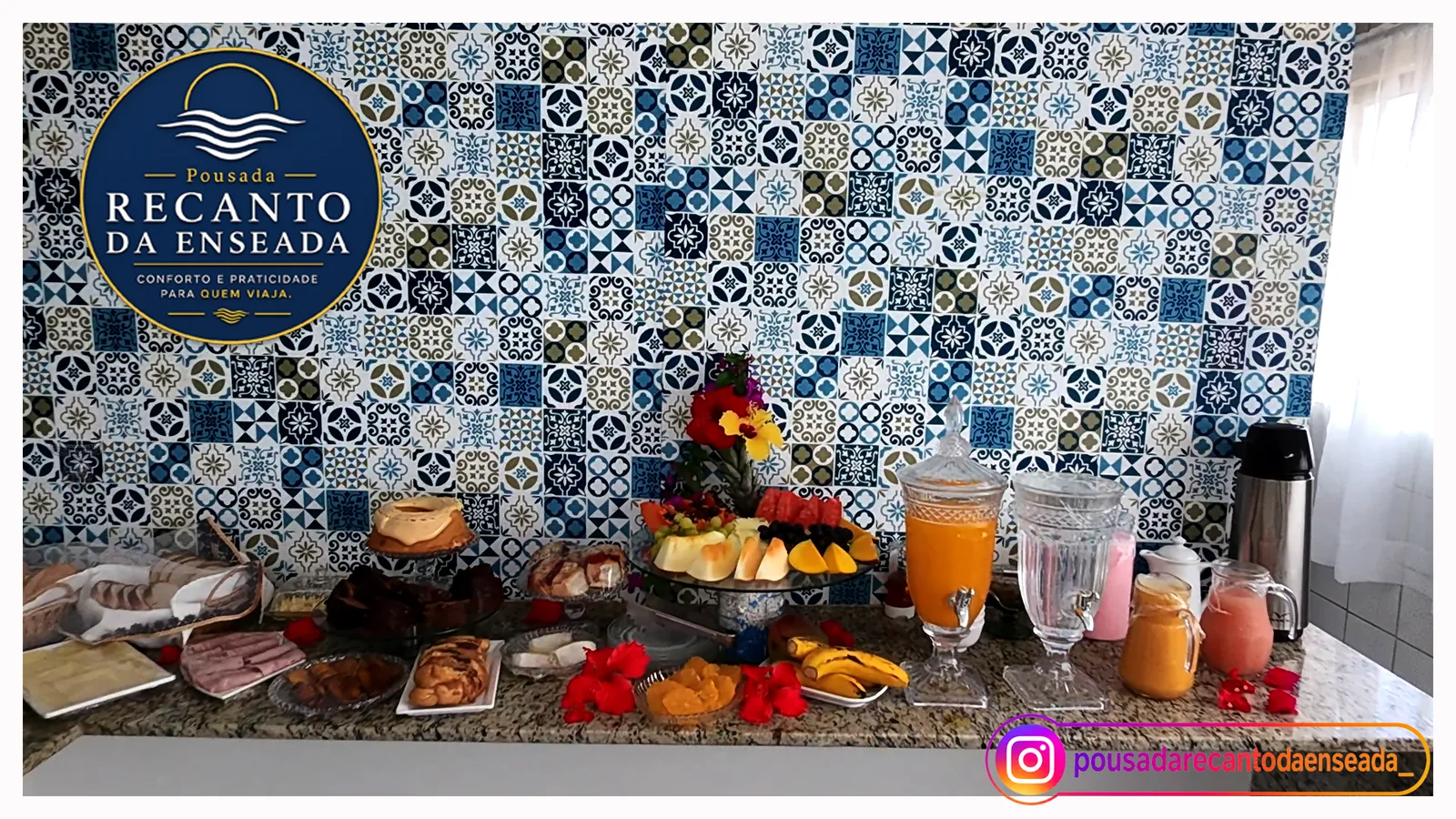 Mesa do café da manhã com frutas, sucos e bolos diante dos azulejos